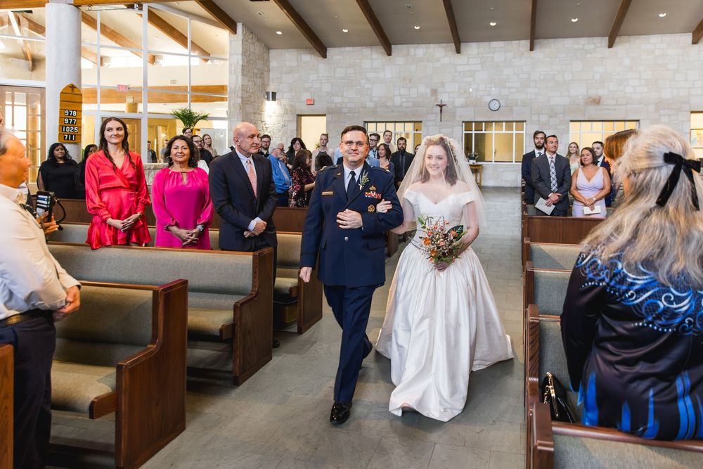 Wedding ceremony processional in modern church interior with wooden pews and white stone walls.