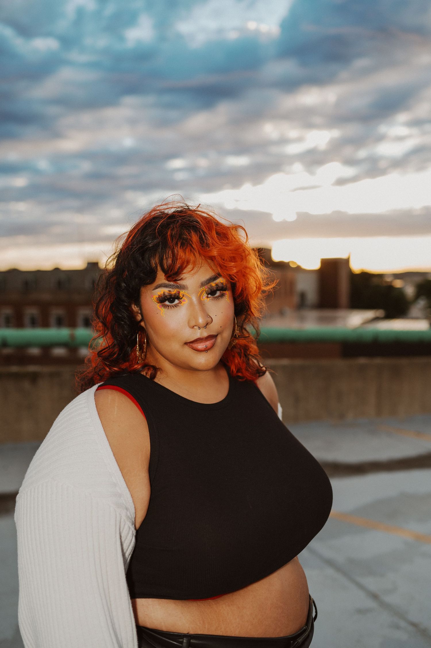 A model in a black and white outfit poses against a cloudy sunset backdrop.