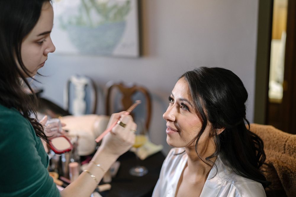 Makeup artist applying cosmetics on a bride-to-be during wedding preparations in a warmly lit room.