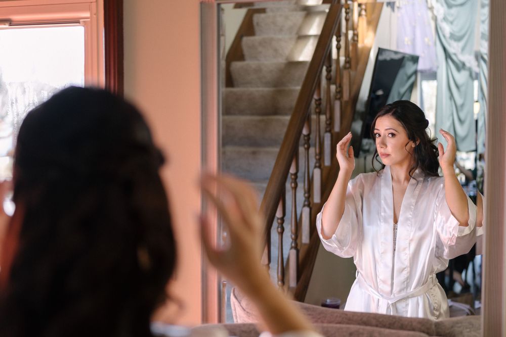 Woman in a white robe applies makeup while looking into a mirror during morning preparation routine.