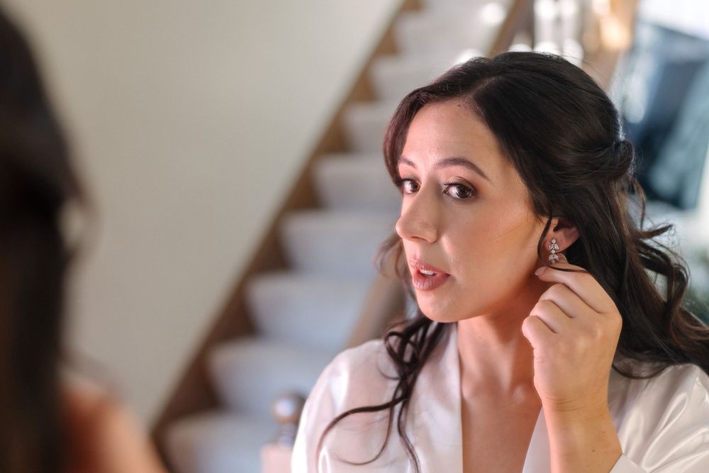 Woman in white robe adjusts her earring while preparing for a special event.