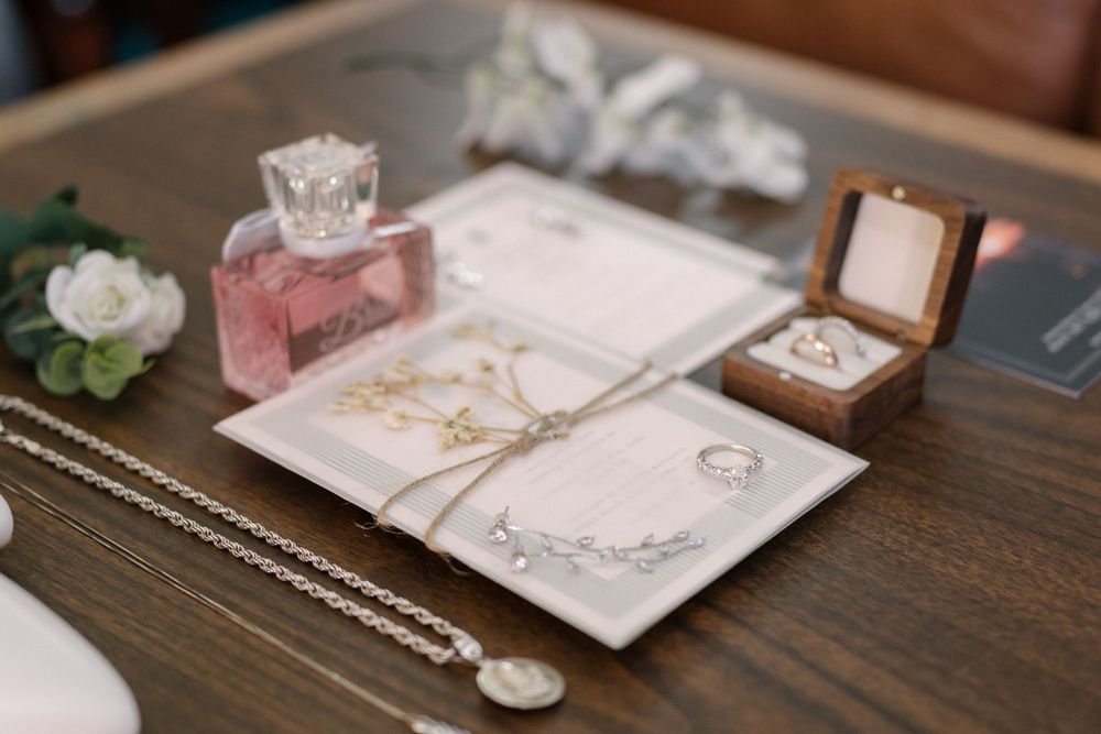Wedding accessories including jewelry, perfume bottle, and invitation cards displayed on wooden surface with floral details.