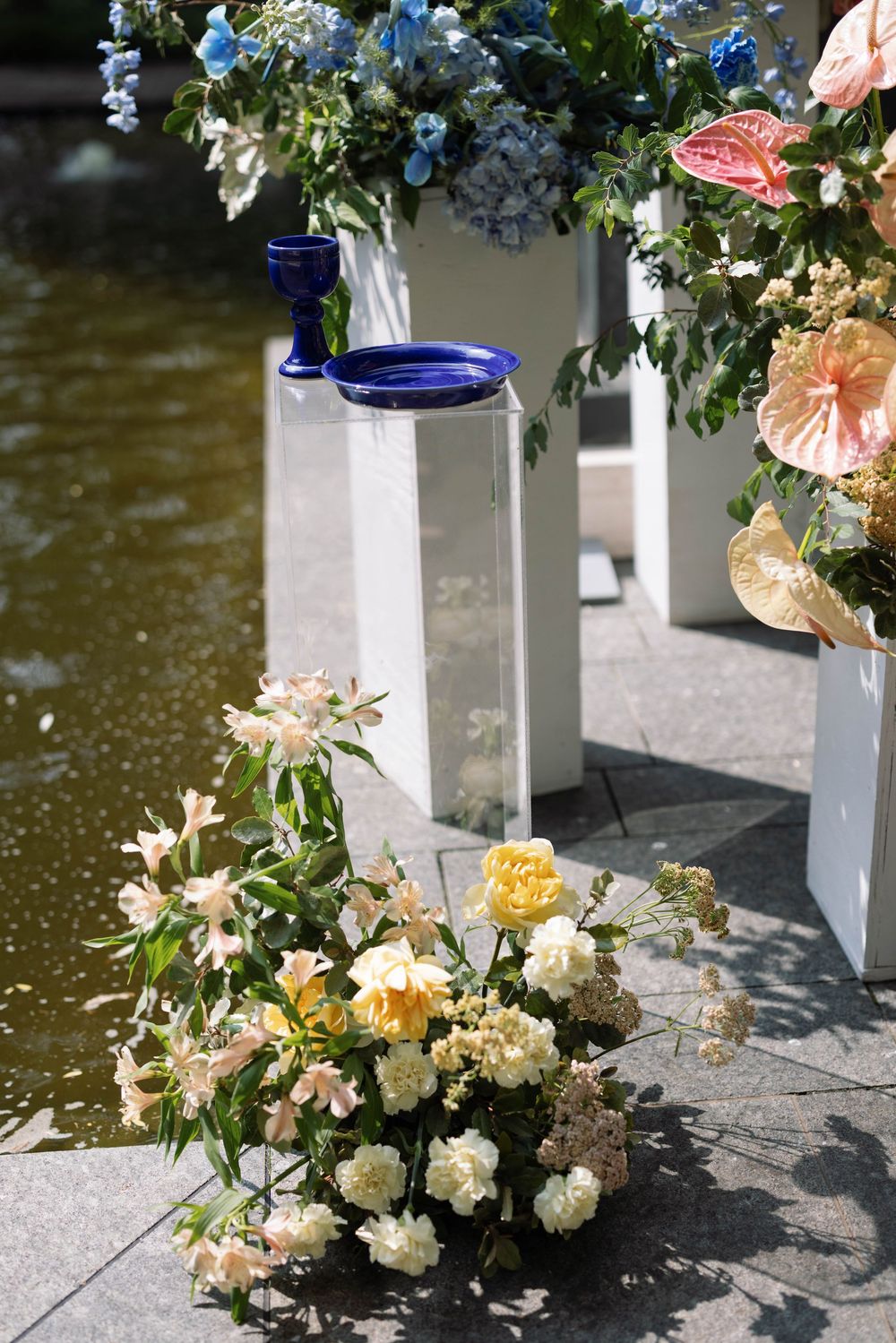 White floral arrangements with yellow roses decorating outdoor wedding venue pillars near water.