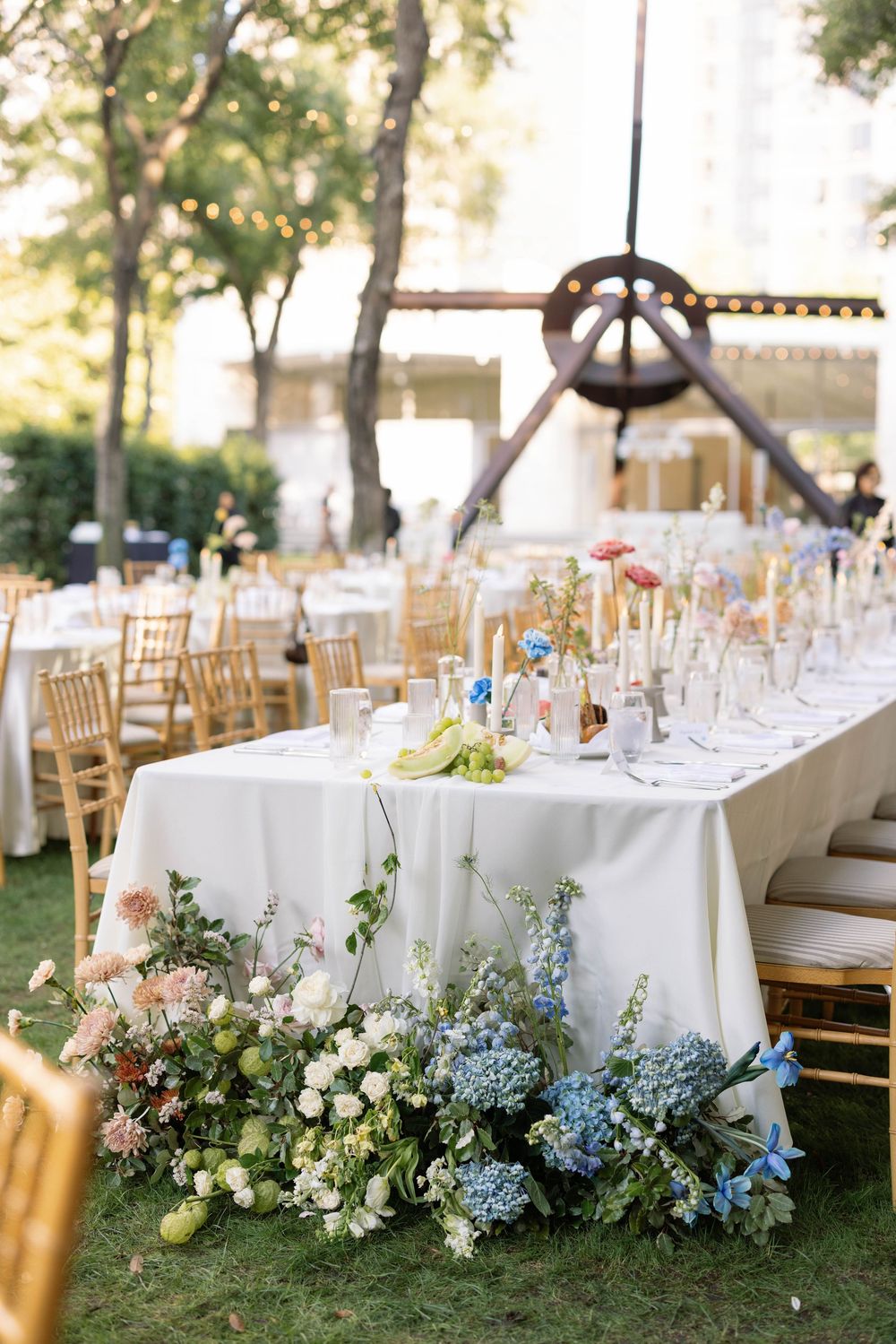 Outdoor wedding reception tables with white linens and lush floral arrangements in pink and blue hues.
