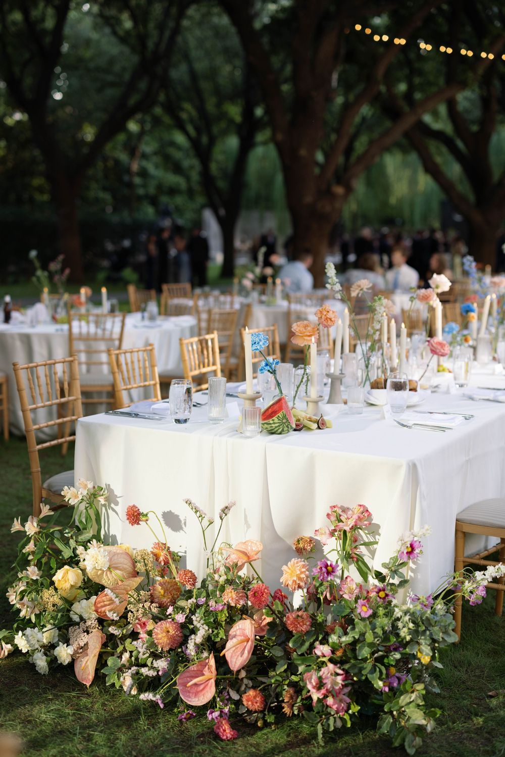 Romantic outdoor wedding reception with white tables adorned with pink floral arrangements under string lights.