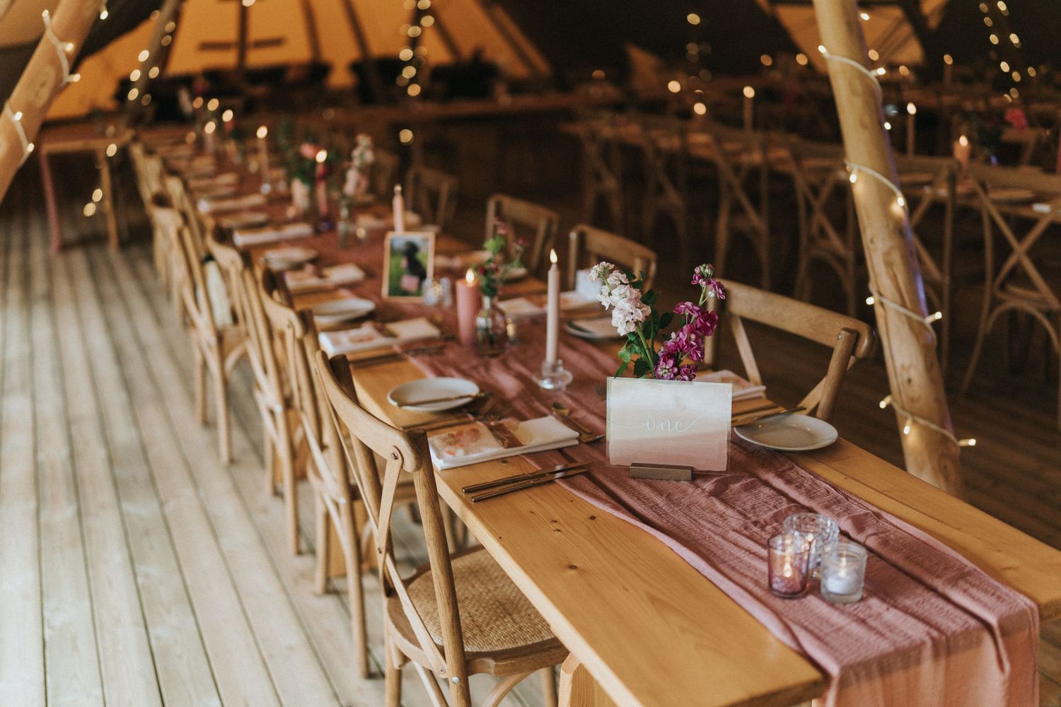 Rustic wooden farm tables with pink runners and cross-back chairs set up for a barn wedding reception at Scrivelsby Walled Garden.