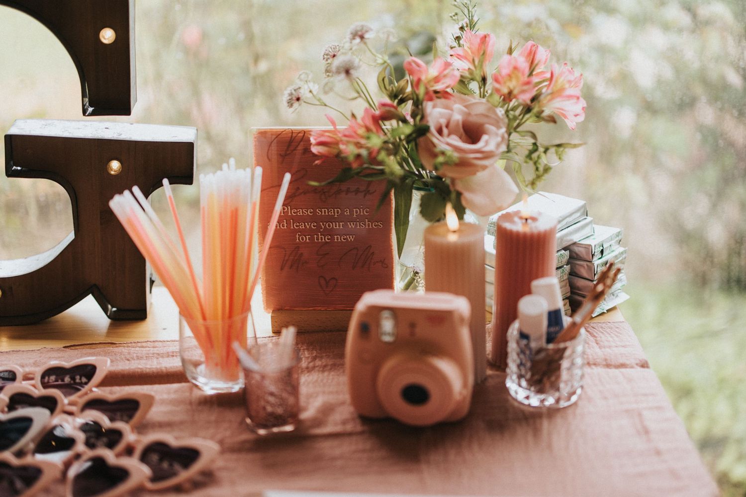 Pink floral arrangement with vintage camera and party decorations on a rustic table setting at Scrivelsby Walled Garden.