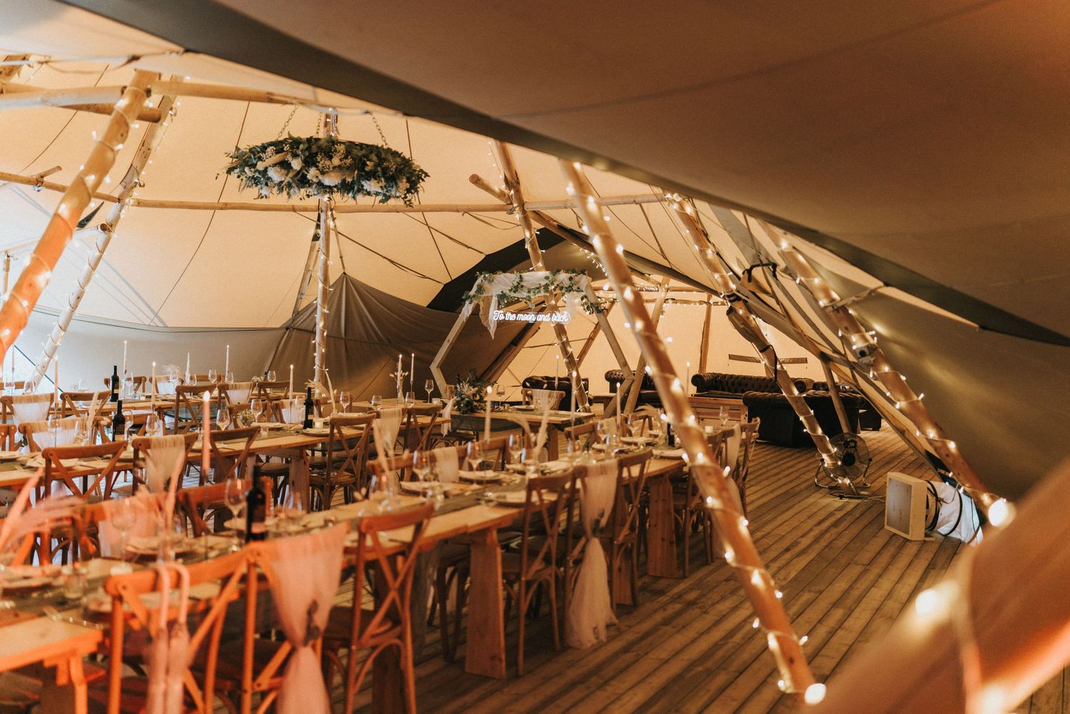 A rustic wooden chandelier with hanging string lights illuminates a cozy interior space with warm amber lighting at Scrivelsby Walled Garden