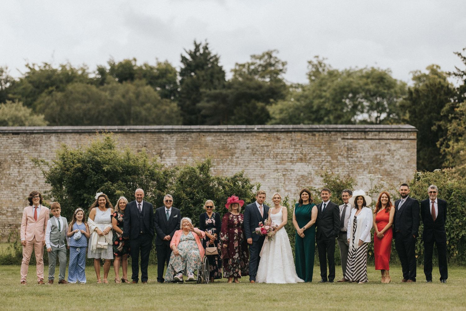 Wedding party lined up against a rustic stone wall for formal group photos in an outdoor garden setting at Scrivelsby Walled Garden.