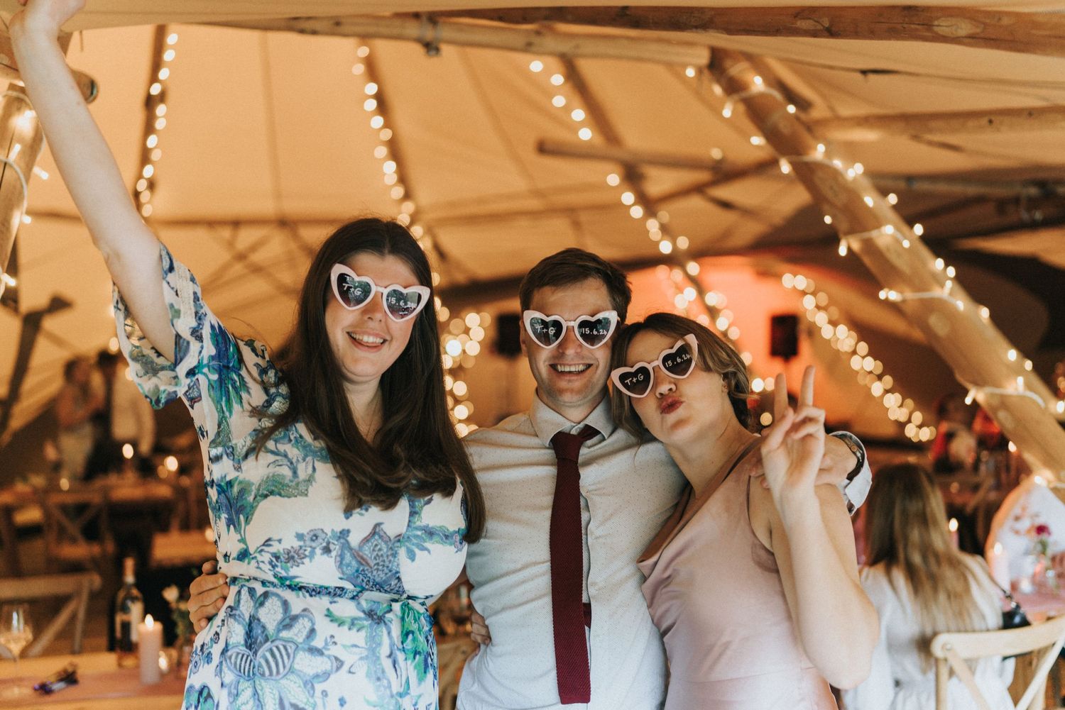 People celebrate at a wedding reception while wearing sunglasses under string lights at Scrivelsby Walled Garden.