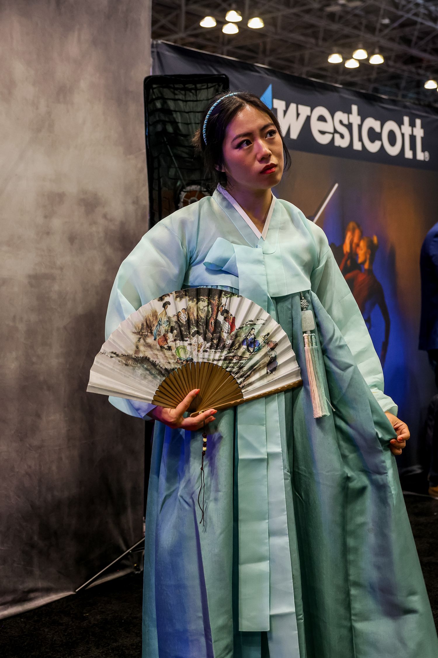 A person wearing a traditional mint green hanbok performs an elegant fan dance under soft lighting.