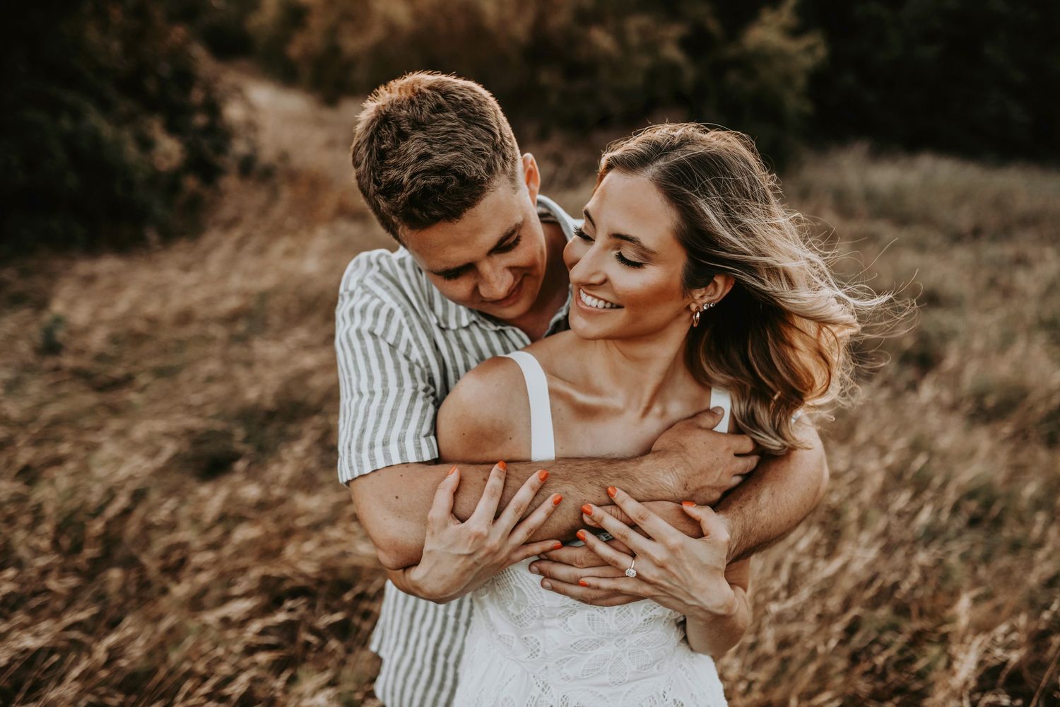 Close-up of couple’s hands intertwined in a dreamy golden field at dusk