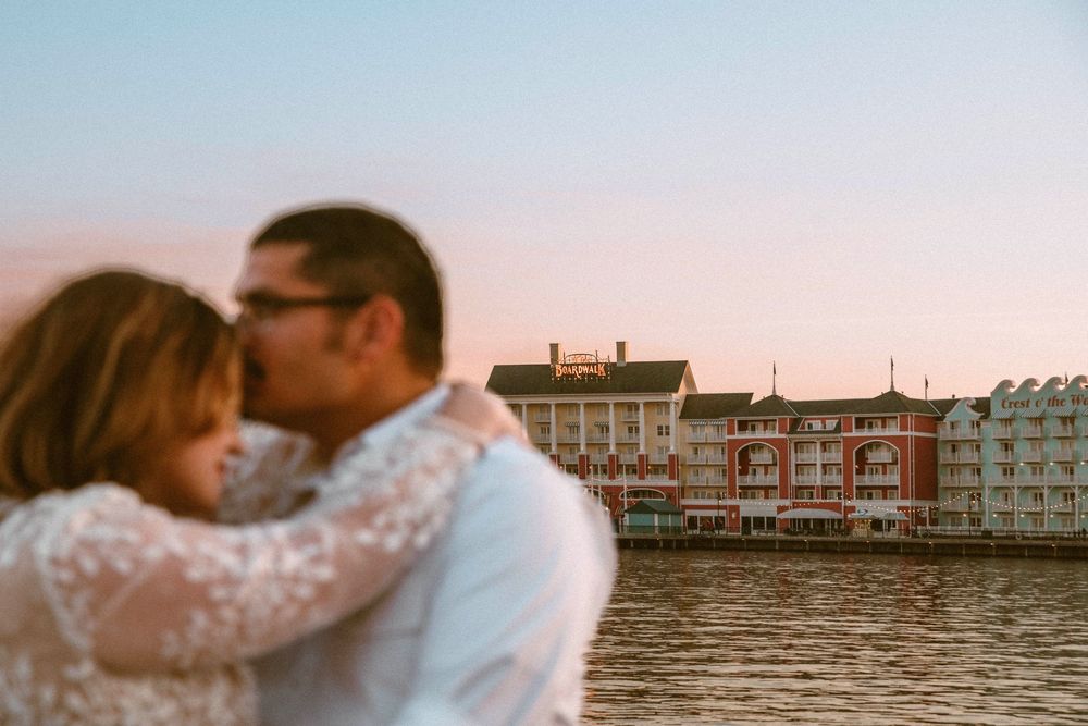 Gillian & Miles' anniversary photos at Disney Boardwalk. Gillian in white lace Ivy City Co dress, boardwalk in distance. Cred: LexTakePix