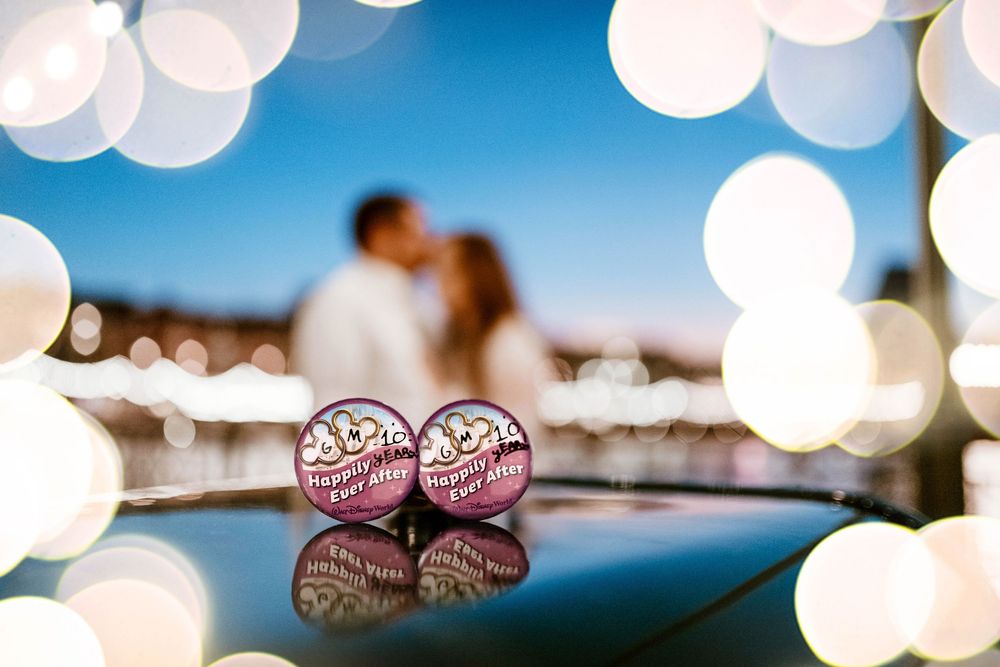 Gillian & Miles' anniversary photos at Disney Boardwalk, blurred in background with "I'm Celebrating" buttons and bokeh. Cred: LexTakePix