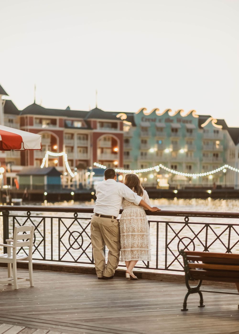 Gillian & Miles' anniversary photos at Disney Boardwalk. Gillian in white lace Ivy City Co dress, looking out over water Cred: LexTakePix