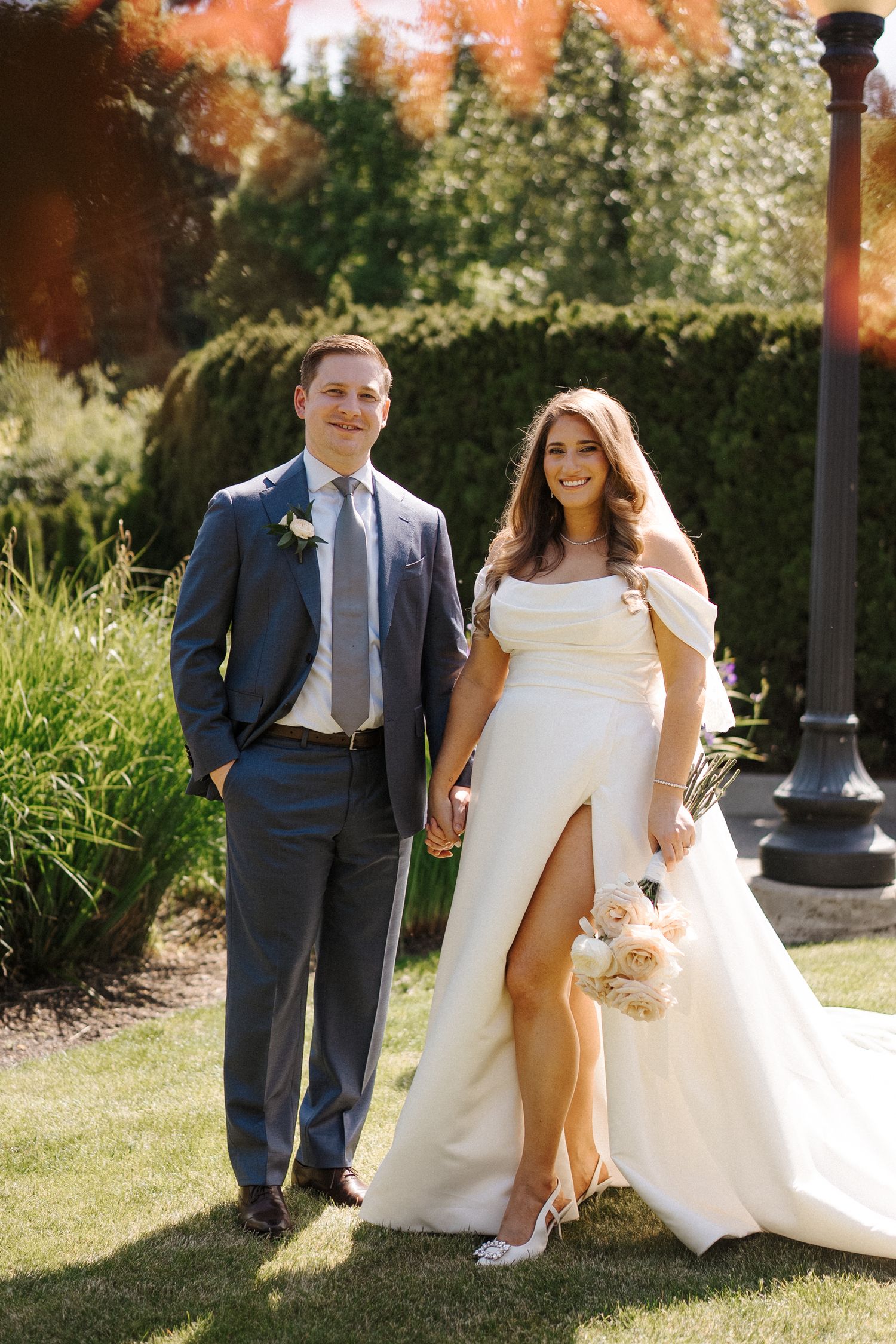 Wedding couple wearing navy suit and white dress share playful candid moments in garden setting during photo session.