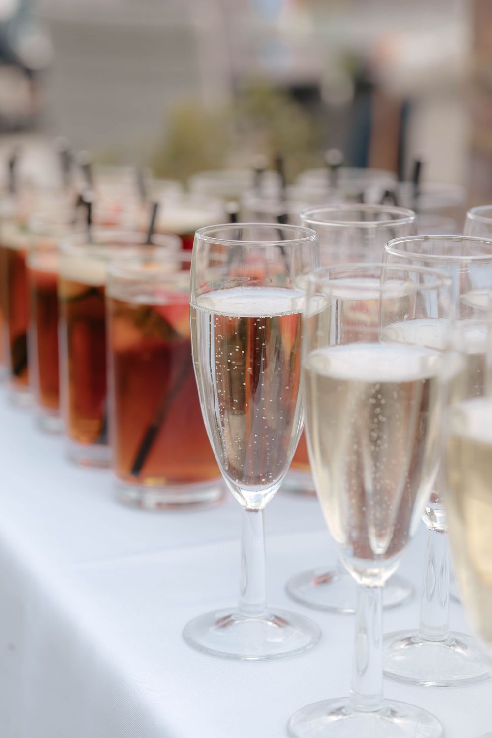 Champagne flutes and wine glasses filled with sparkling drinks on a white tablecloth at an elegant event.