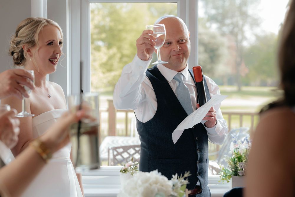 Wedding toast during outdoor reception as celebrants raise their glasses on a sunlit porch.
