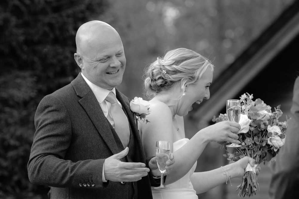 Black and white wedding photo showing a joyful shared moment between a person in a suit and one in a wedding dress.