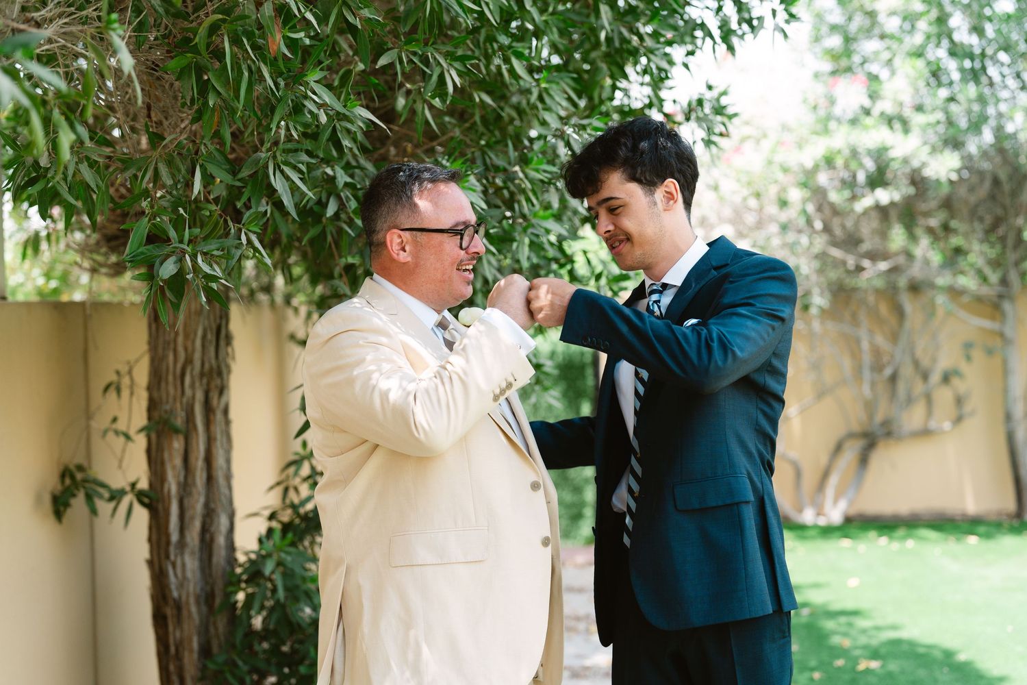 Two people in formal attire sharing a special moment in a garden setting with greenery in the background.