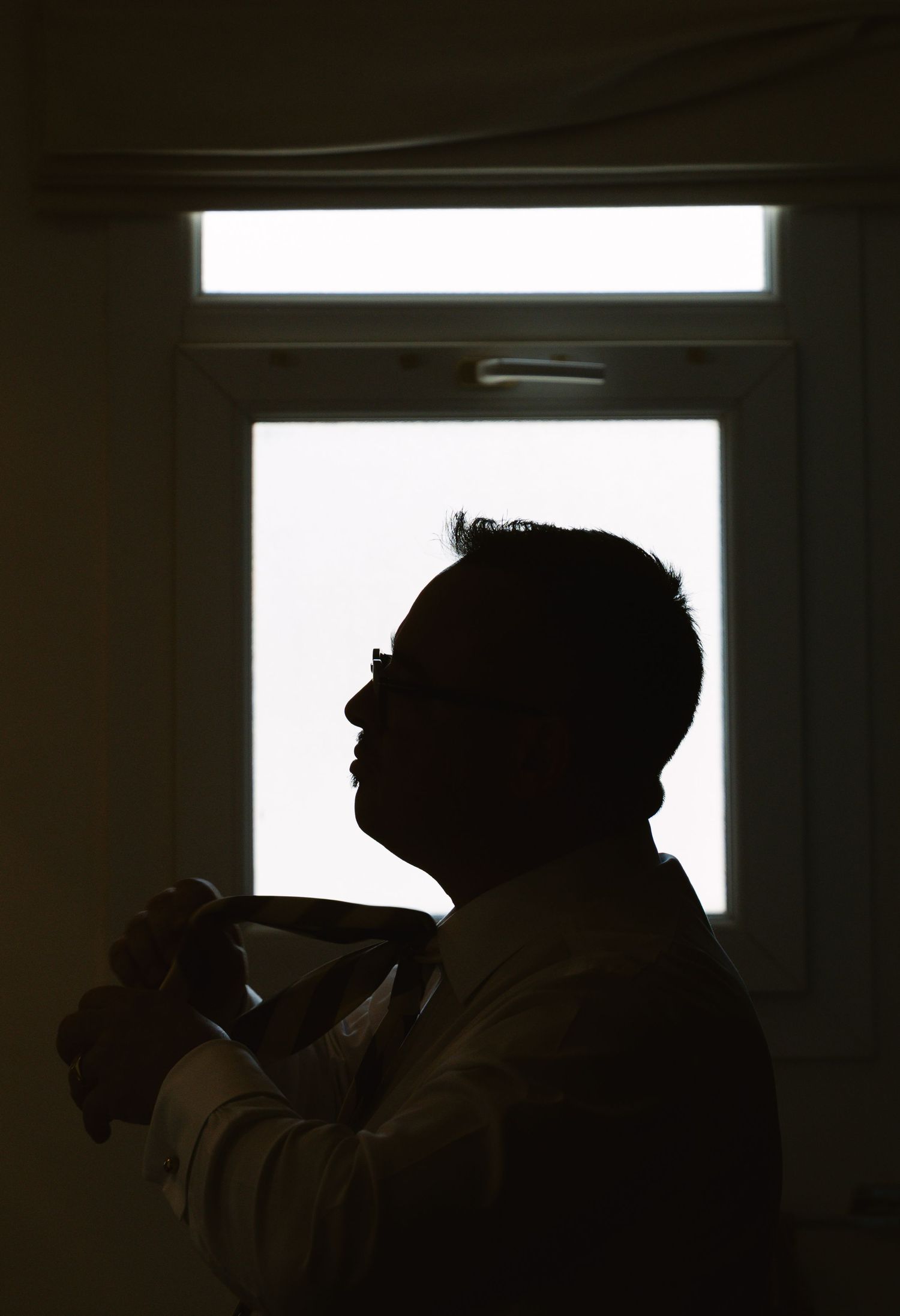 A silhouetted figure holds a cup while standing in front of a bright window, creating a dramatic backlit profile shot.