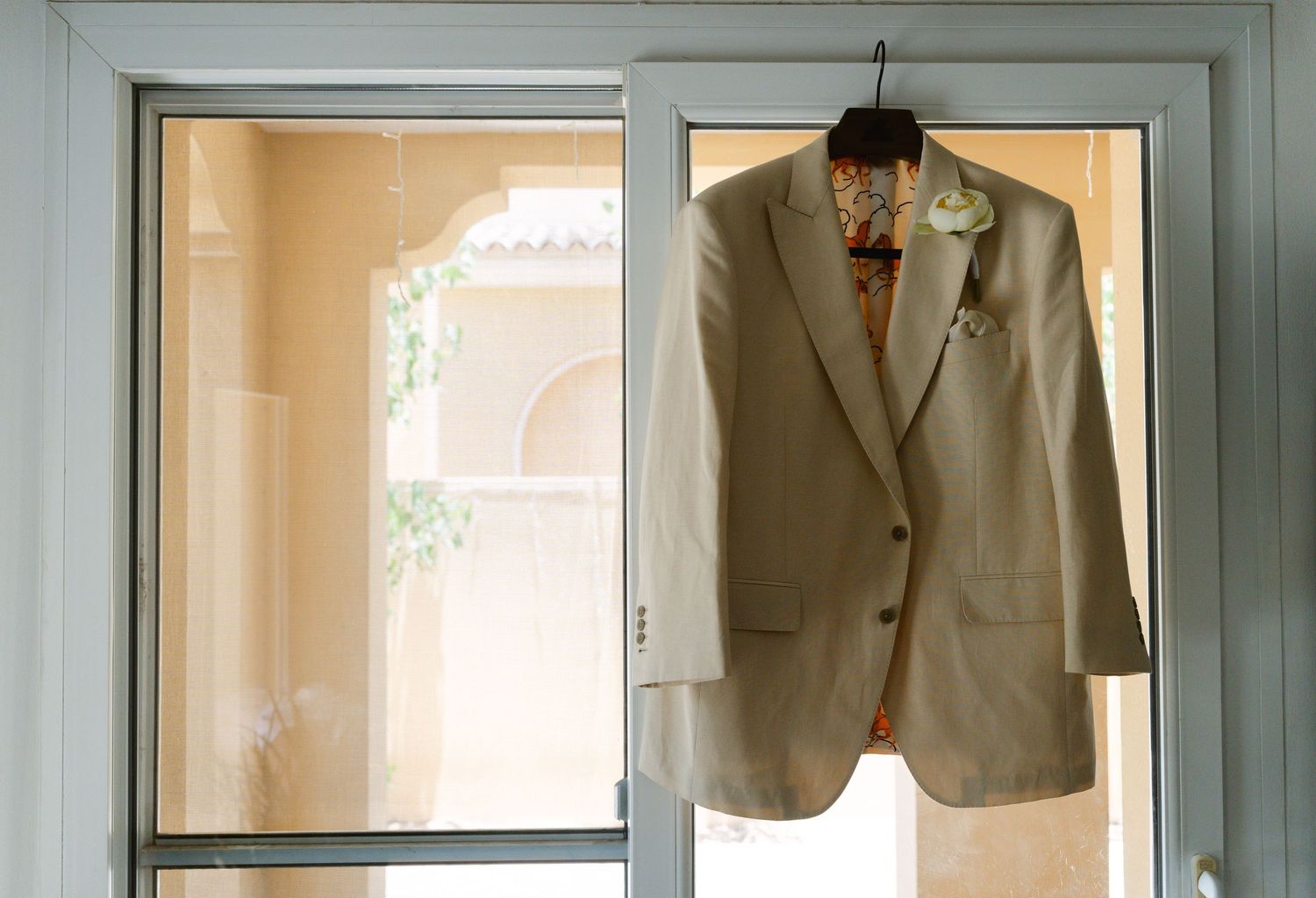 A row of tan and beige formal suit jackets hanging neatly in mirrored closet storage spaces.