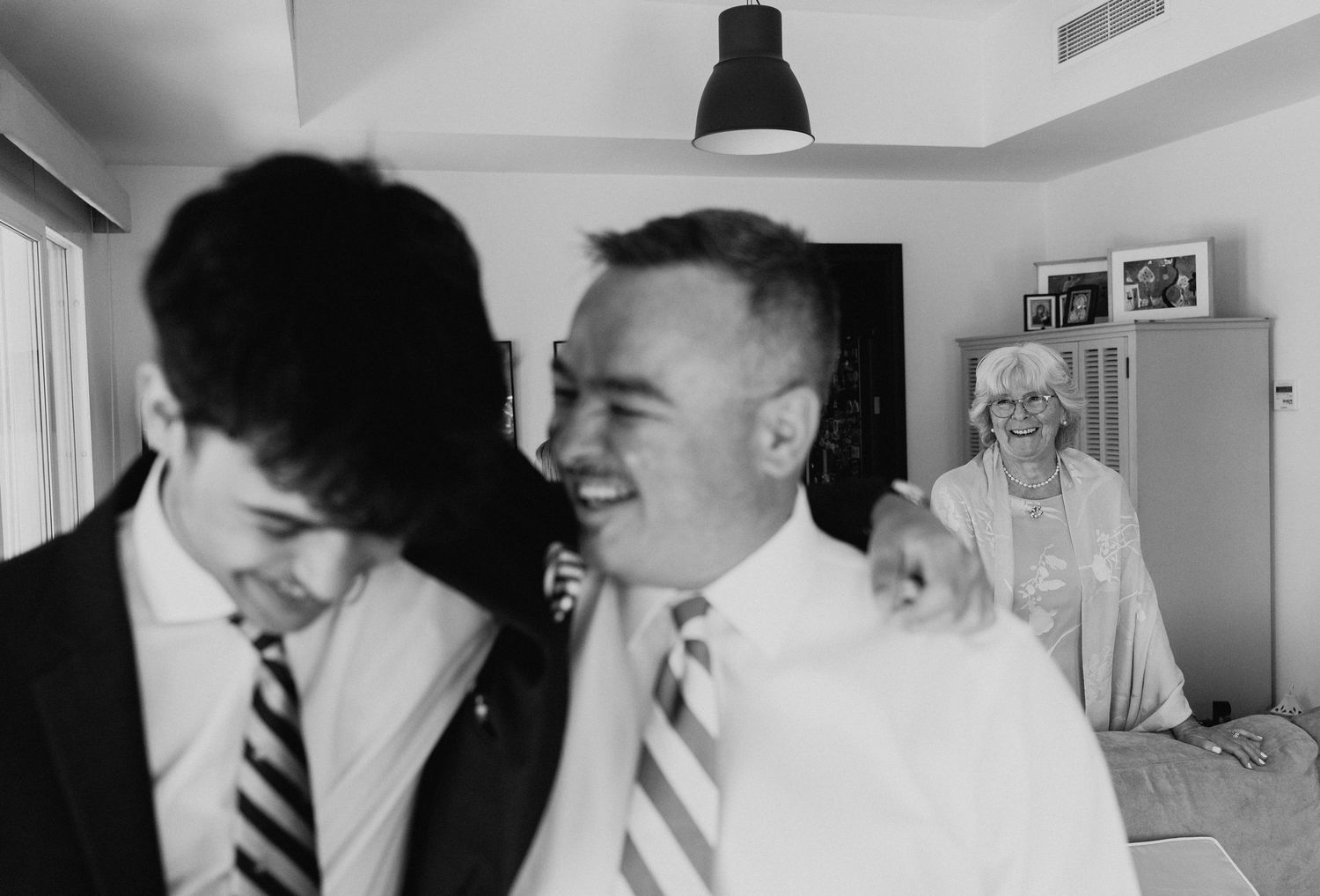A vintage black and white photograph showing people in ties and formal wear inside a room with a pendant light.