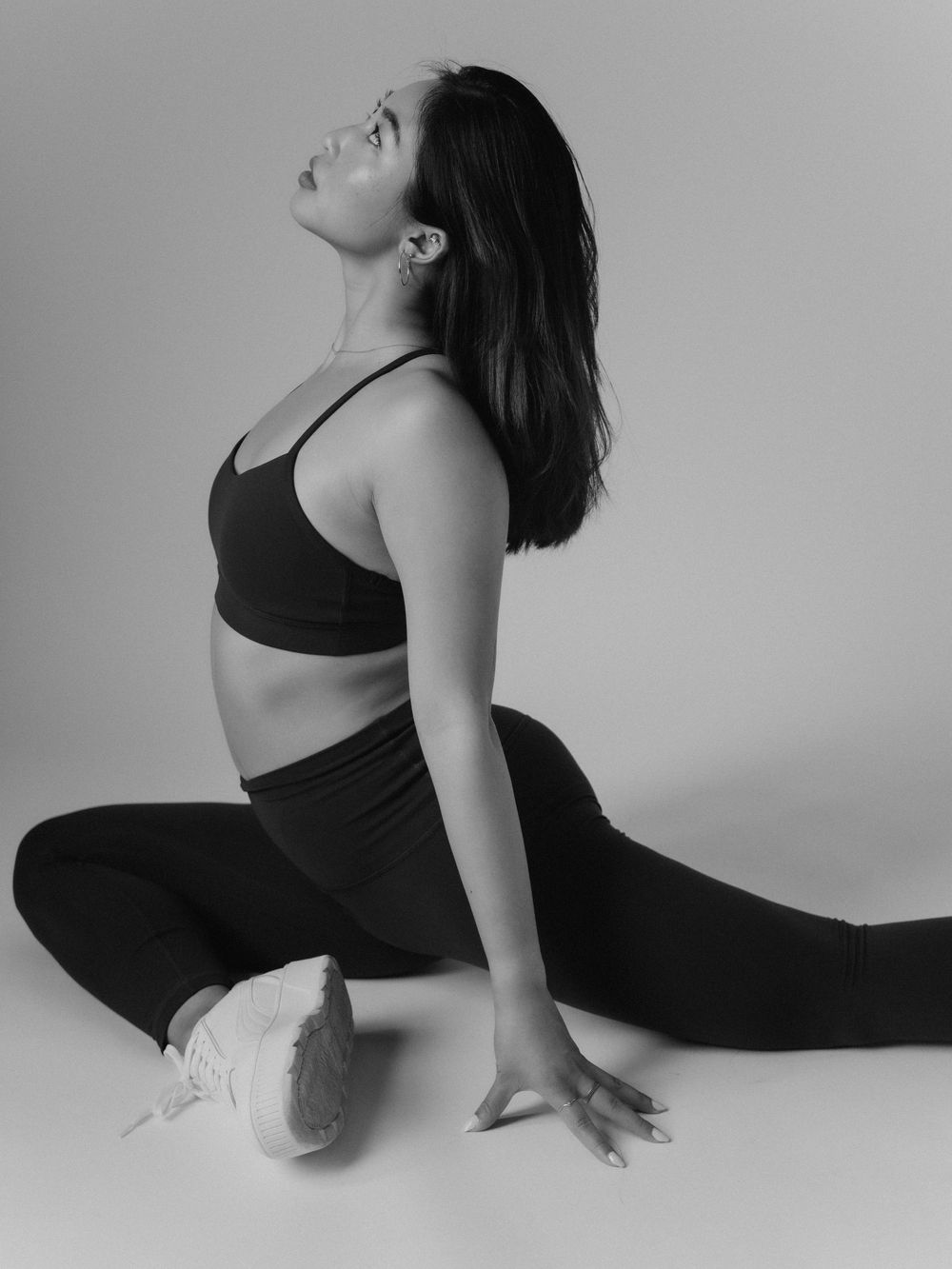Person in black athletic wear performs a pigeon pose stretch on a white background in black and white style.