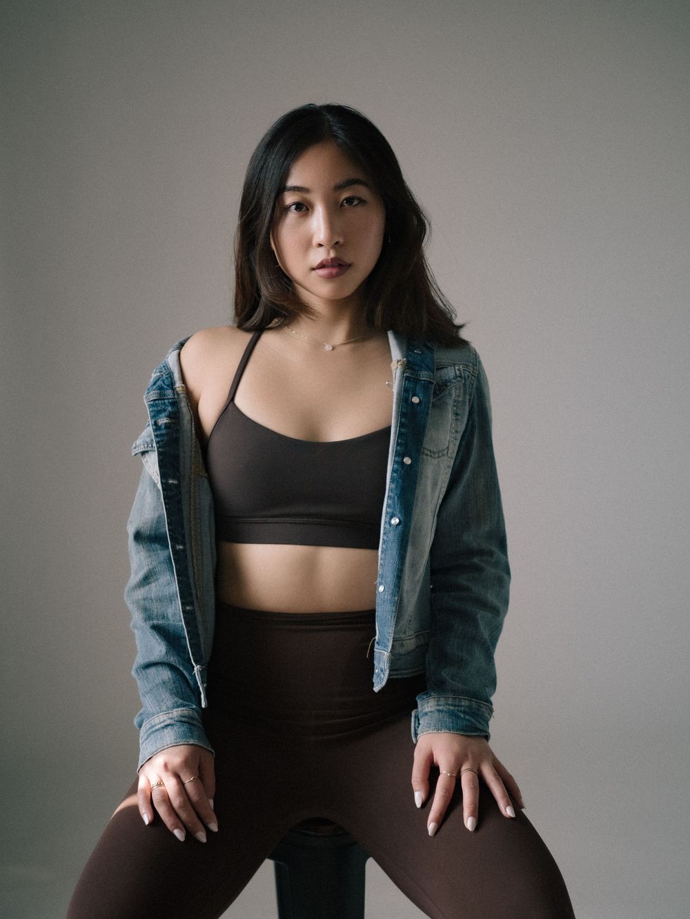 Model in athletic wear strikes casual pose wearing black crop top and denim jacket against neutral background.