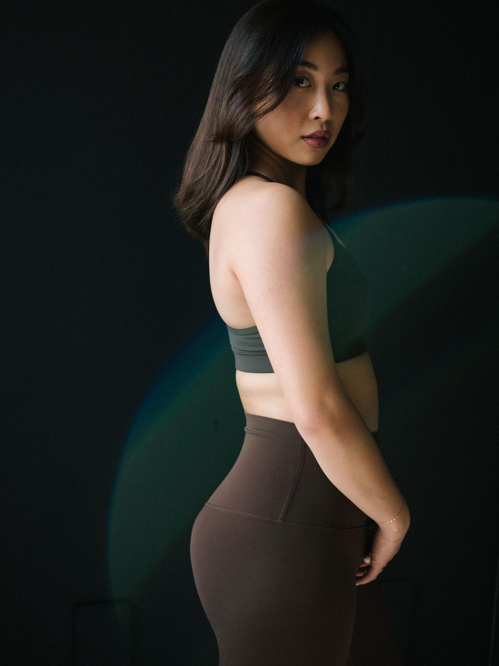 Woman in athletic wear poses against dark background with dramatic lighting and green accents.