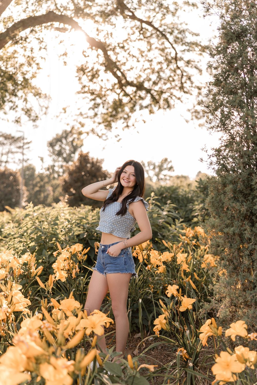 A summer portrait in a garden with yellow daylilies during golden hour as sunlight filters through tree branches.