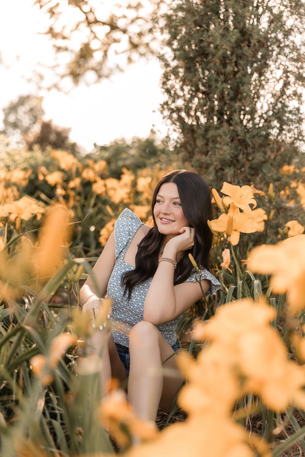 Outdoor portrait in a meadow of yellow flowers with warm sunset lighting creating a dreamy summer atmosphere.