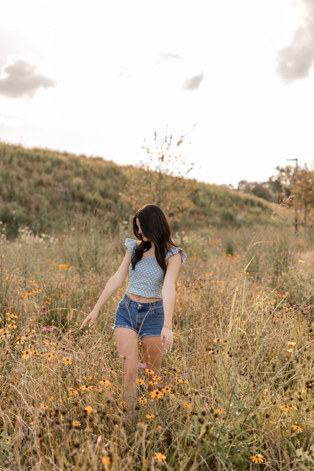 Summer portrait in a wildflower field at golden hour showing denim shorts and a blue cropped top.