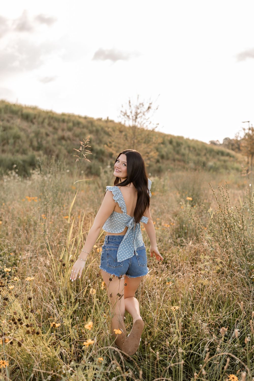 A candid outdoor portrait amidst wild grasses and flowers on a hillside during sunset.