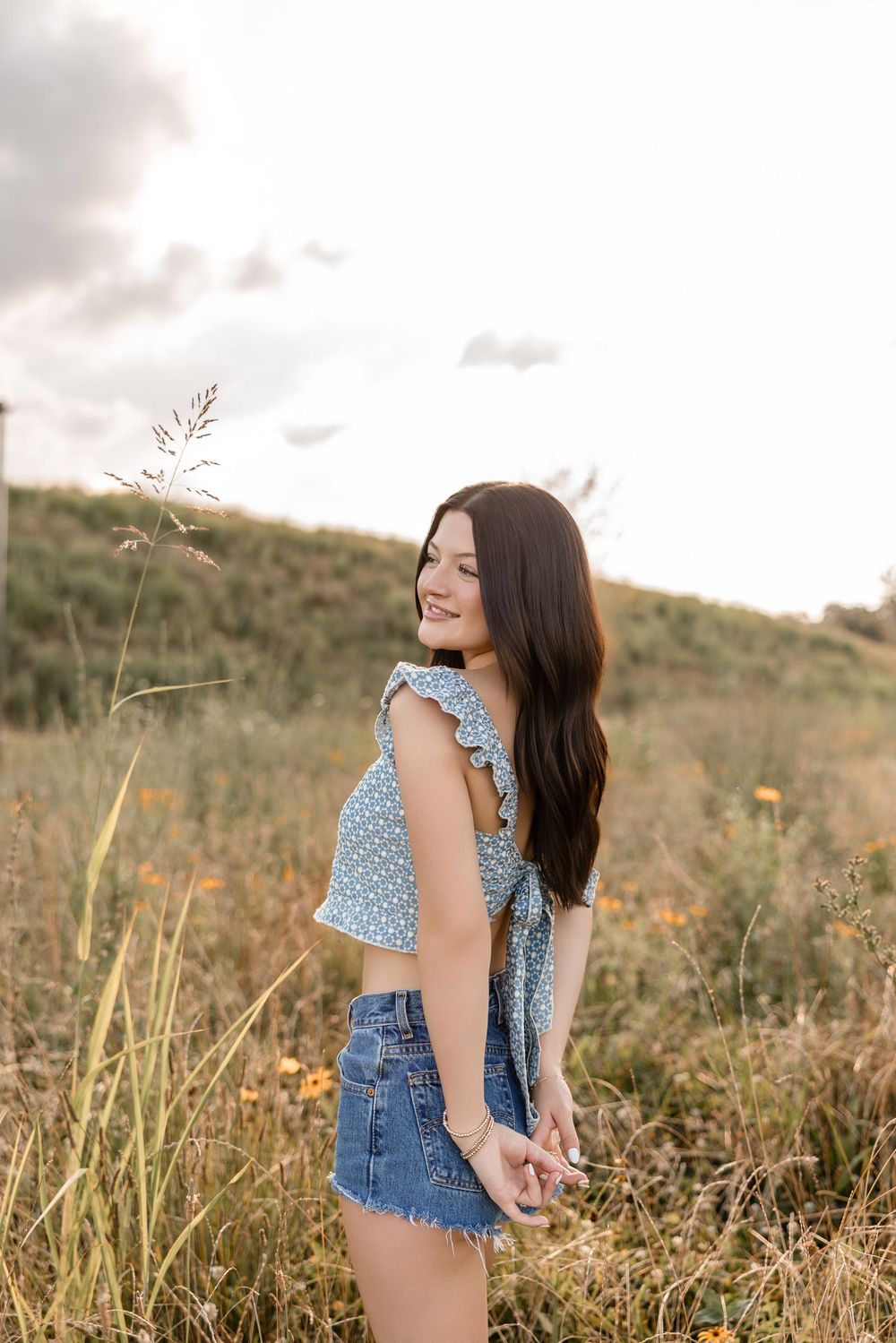 Woman in a polka dot top and denim shorts enjoying a sunny day in a field of tall grass at golden hour.