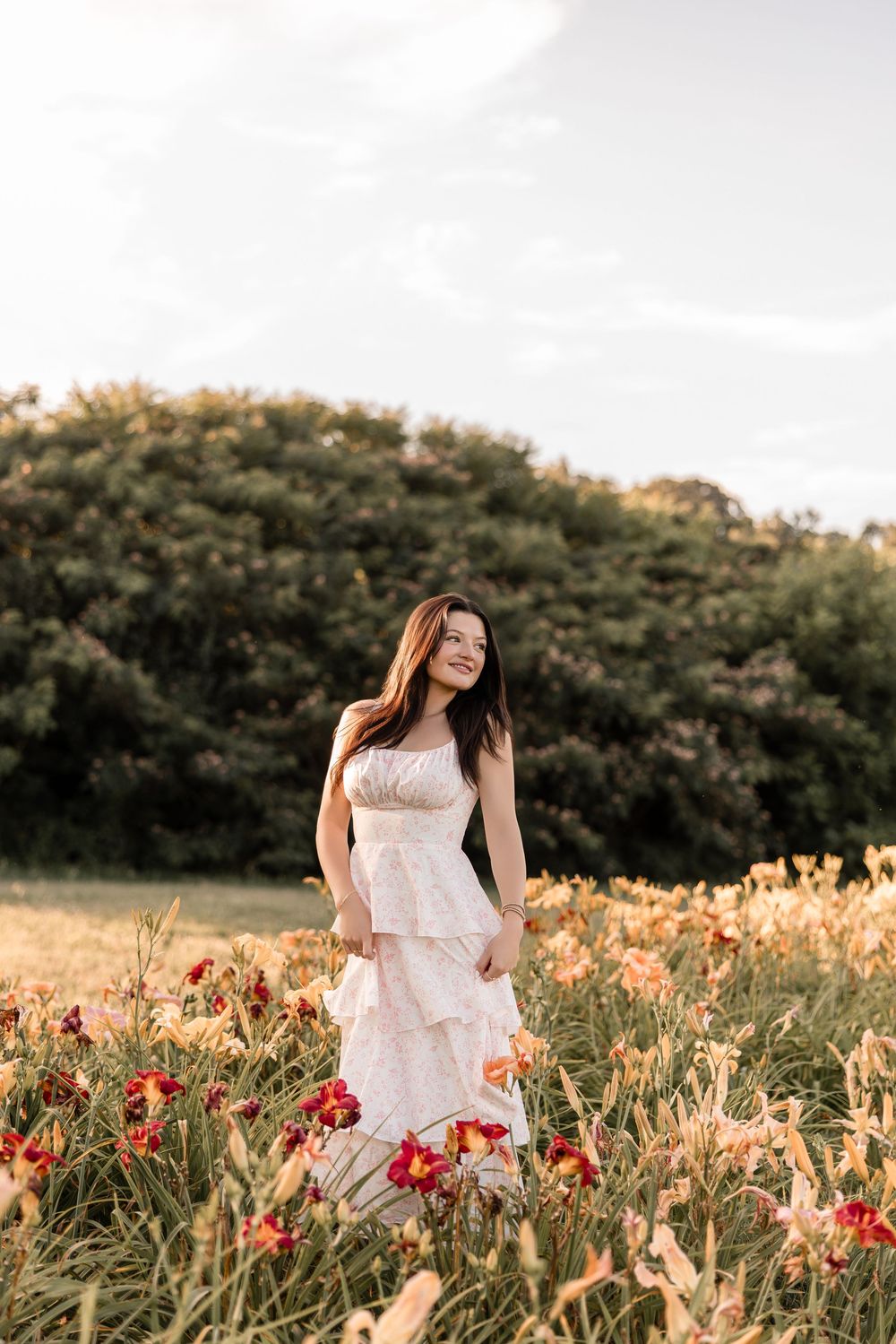 Ethereal portrait in a flower field featuring a flowing white tiered dress among orange and red blooms at dusk.