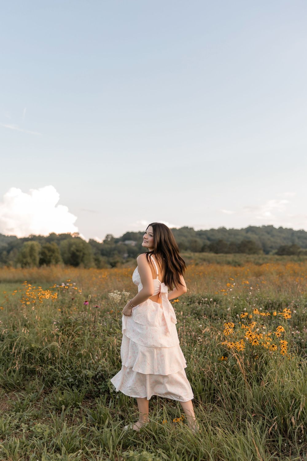 A person in a white tiered dress dances through a wildflower meadow at golden hour.