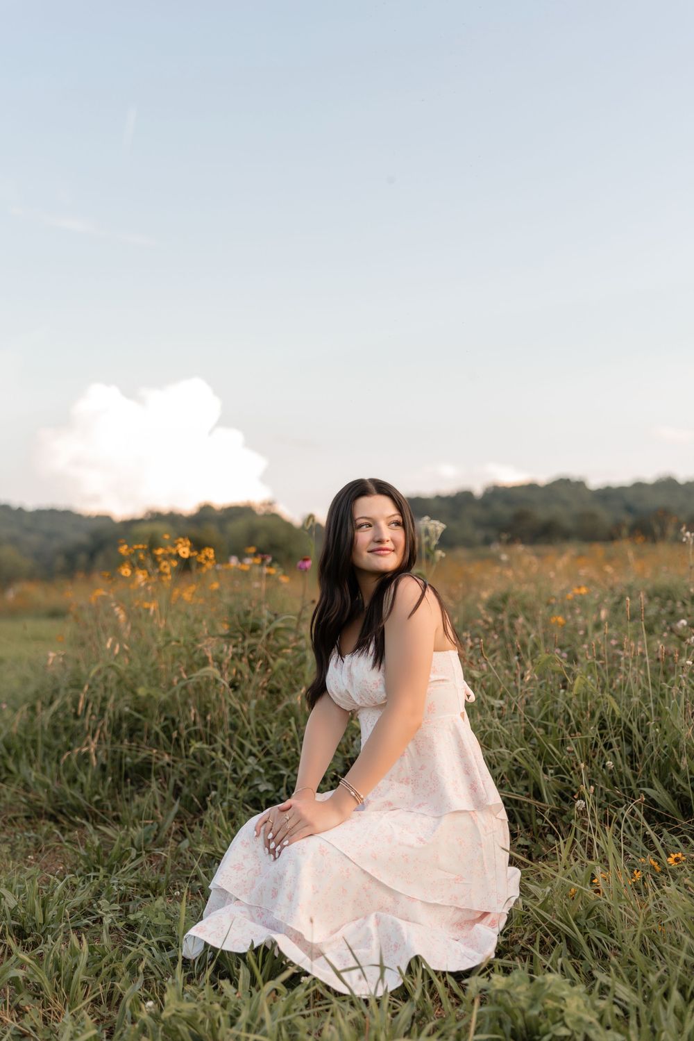 A woman in a white dress sits gracefully in a golden meadow during sunset.
