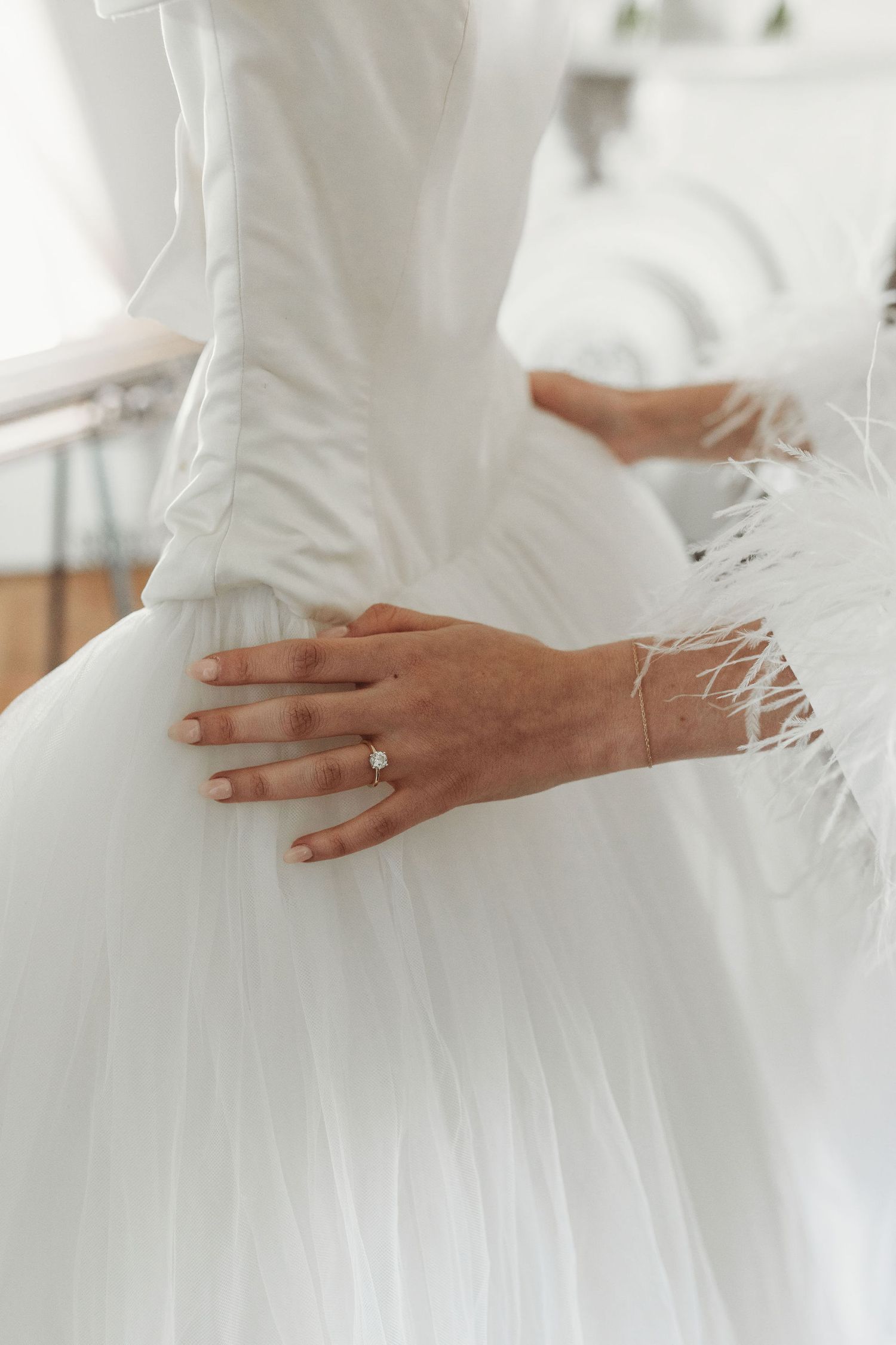 Close-up view of hands touching delicate white tulle fabric texture of a wedding gown skirt.