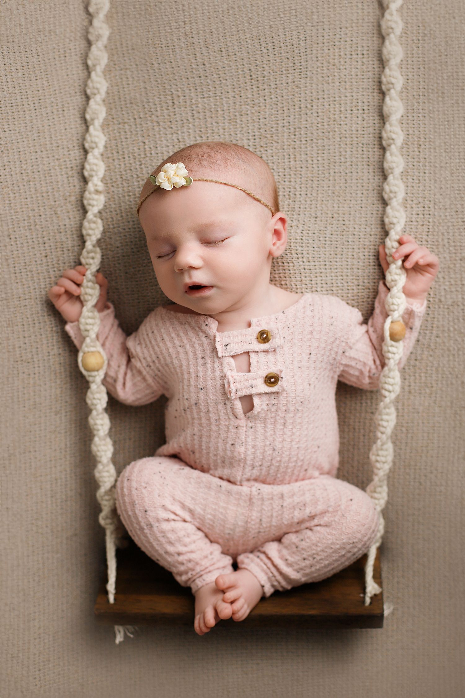 Tiny baby in pink knit outfit sleeps peacefully on a miniature wooden swing with macrame rope details. Utah newborn photography