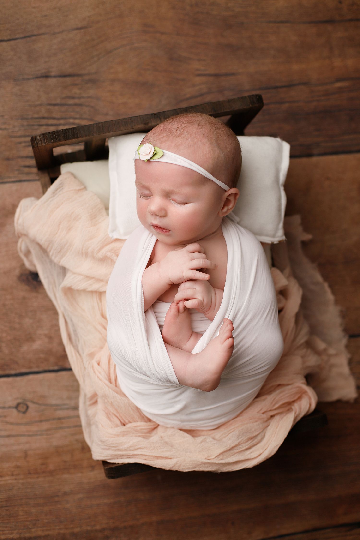 A sleeping newborn wrapped in soft white fabric and peach tulle lies peacefully in a rustic wooden box. Utah newborn photographer