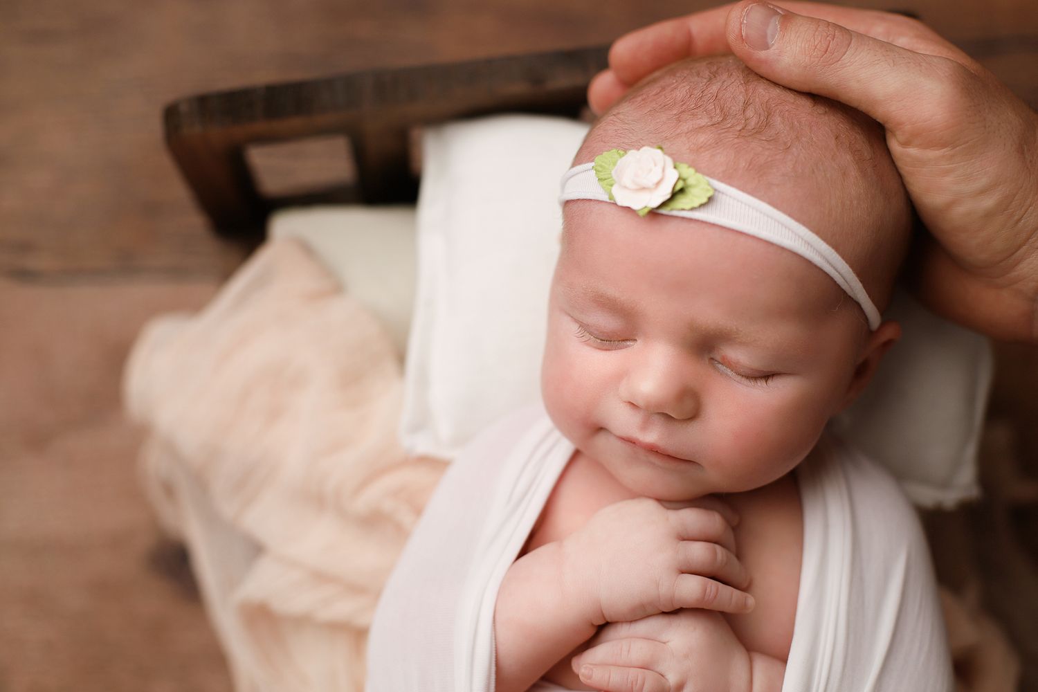 Peaceful sleeping newborn baby wearing white wrap and delicate headband resting on wooden surface. Orem newborn photographer
