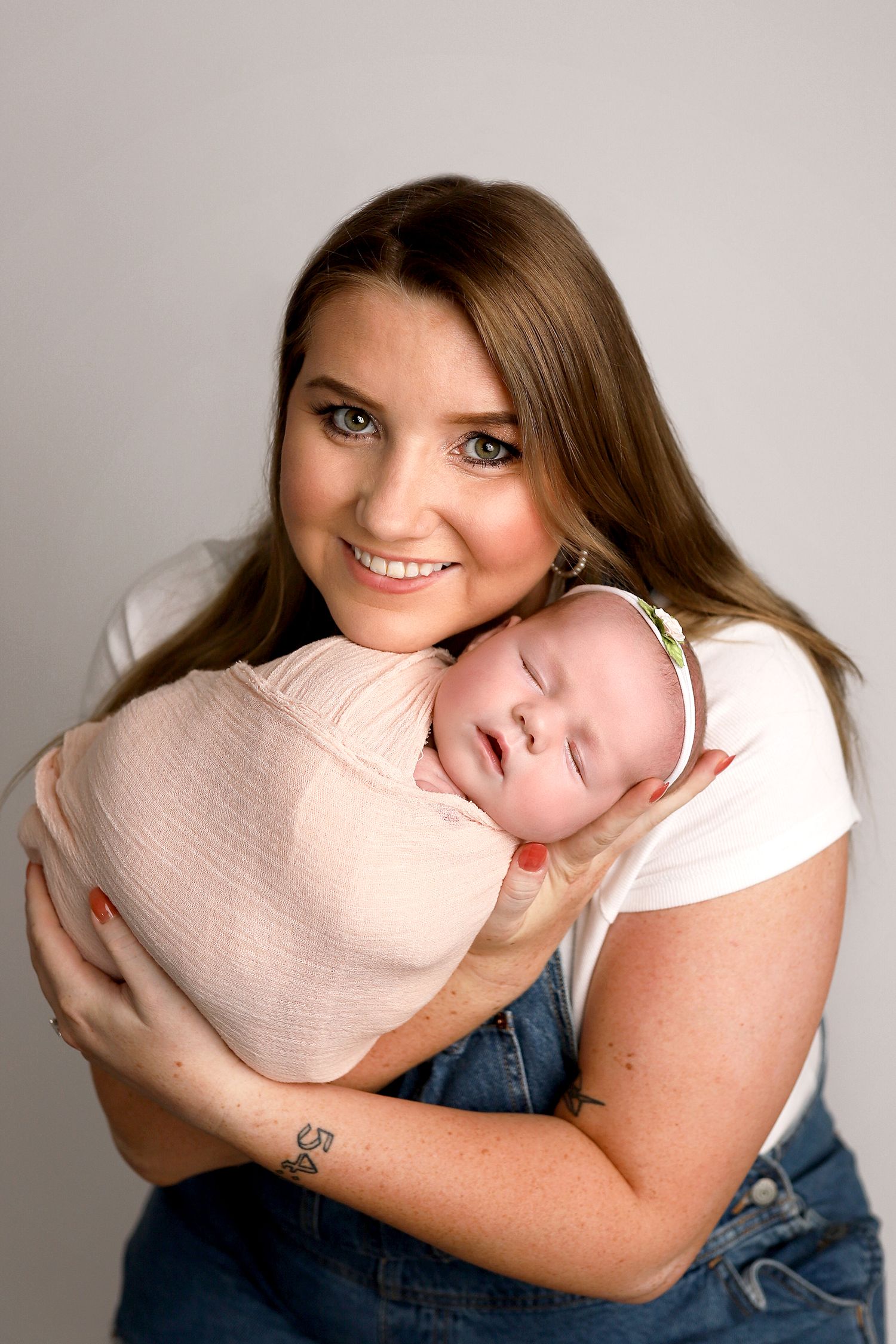A loving mother wearing a white shirt cradles her sleeping baby swaddled in pink during a portrait session. Orem studio.