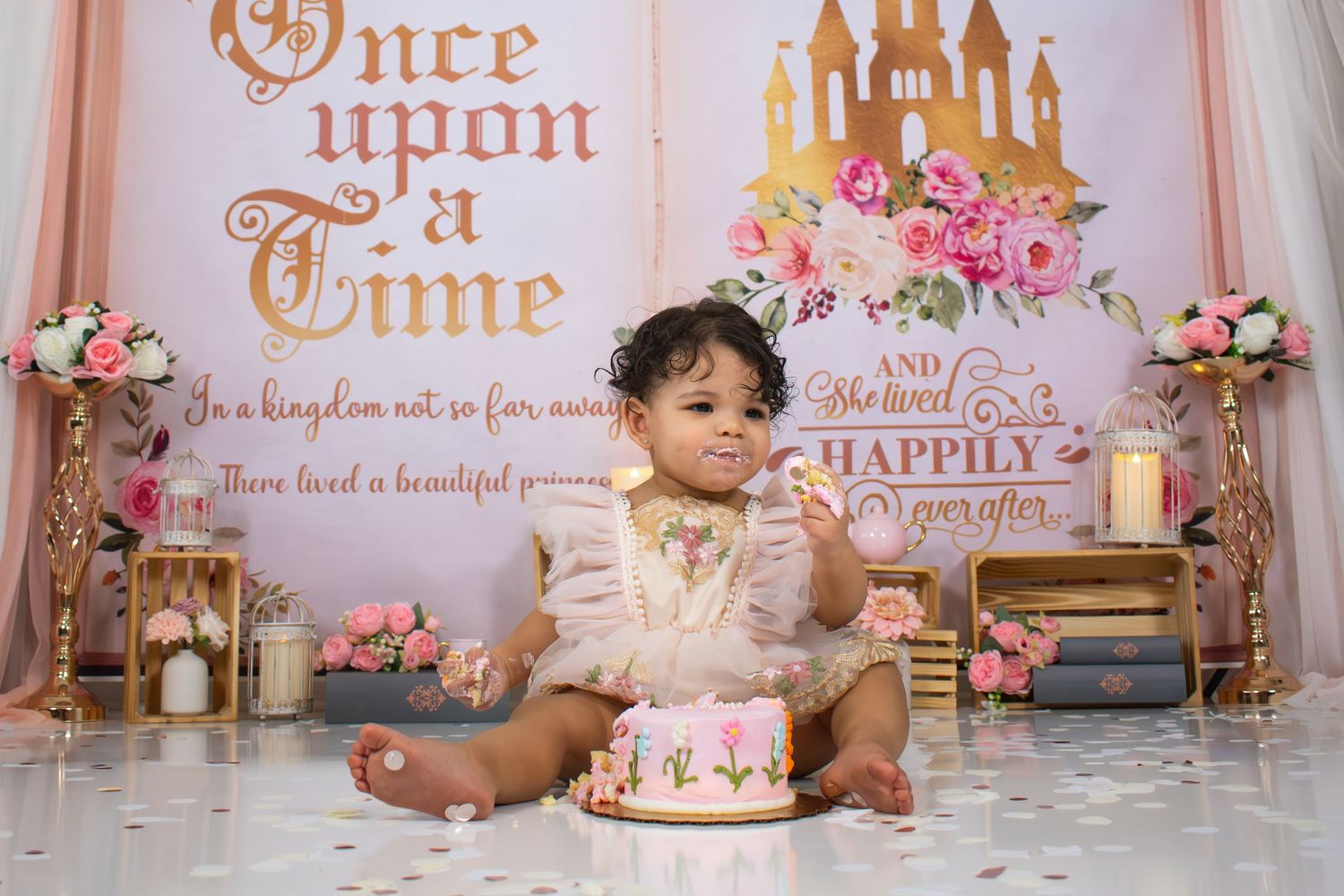 A fairy tale themed first birthday cake smash setup with pink and gold decor featuring a castle backdrop and floral accents spartanburg