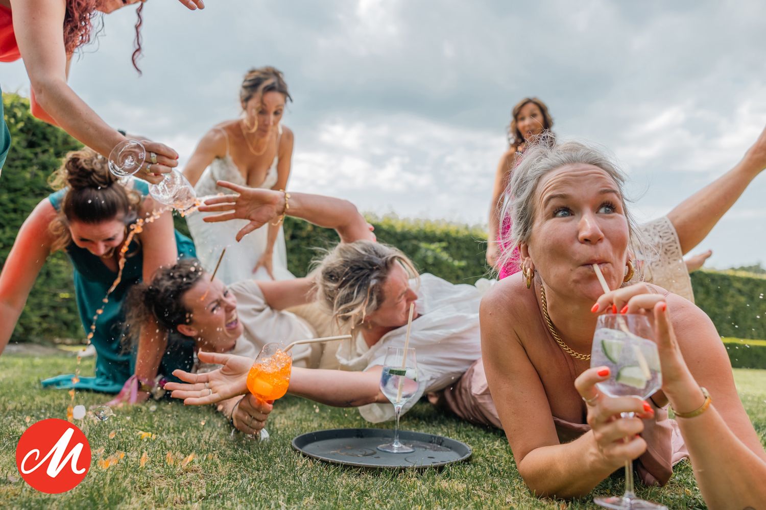 Fun outdoor wedding celebration with guests lounging on grass with drinks.