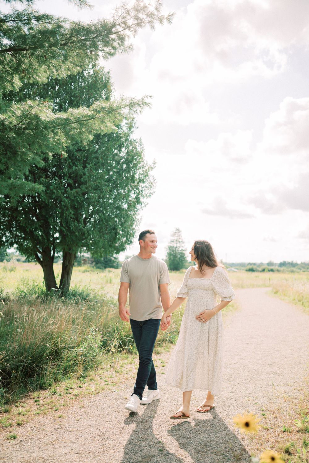 Romantic couple strolling hand in hand on a sunlit nature path with trees in background.