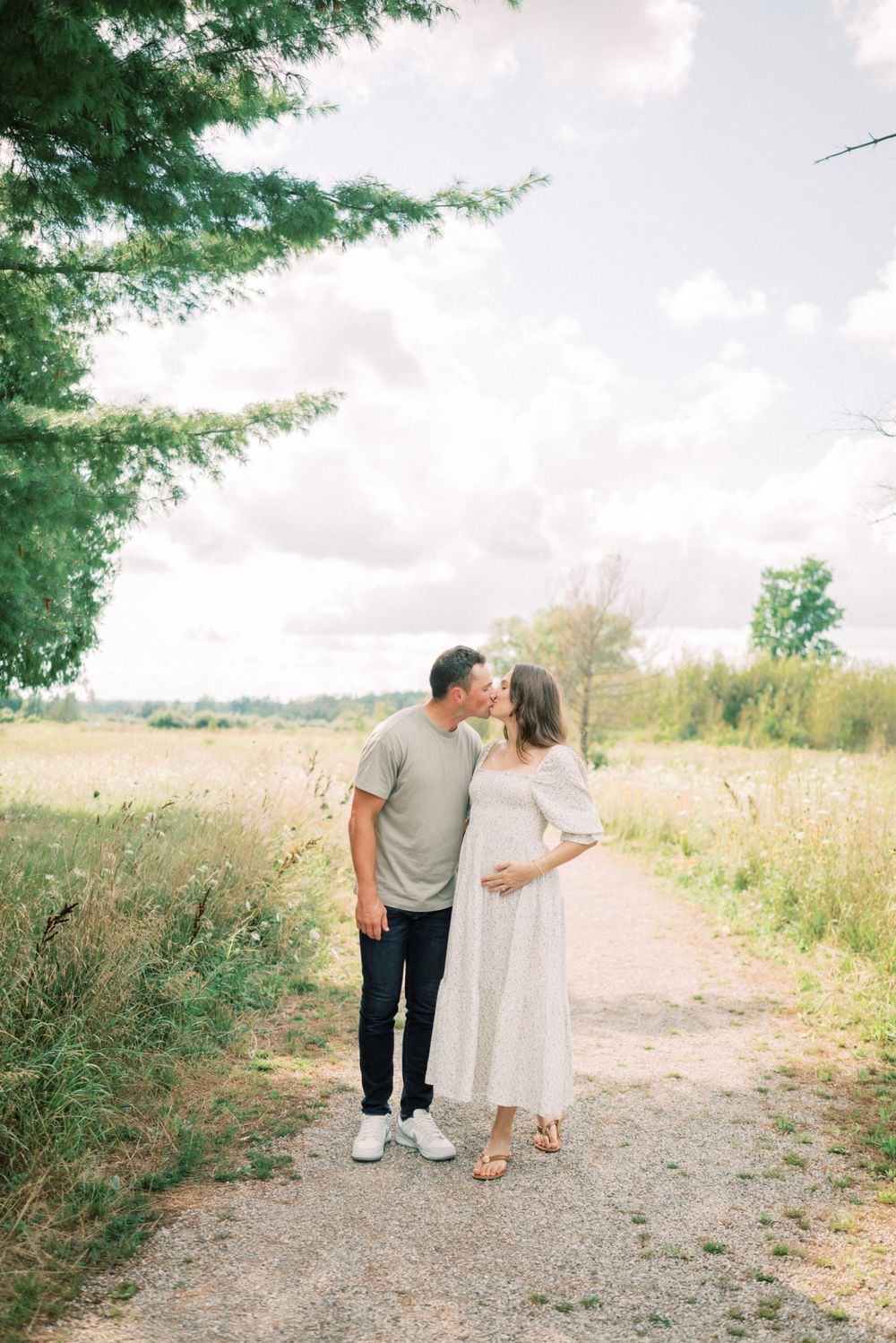 Intimate moment between couple on a nature trail with golden sunlight filtering through trees.