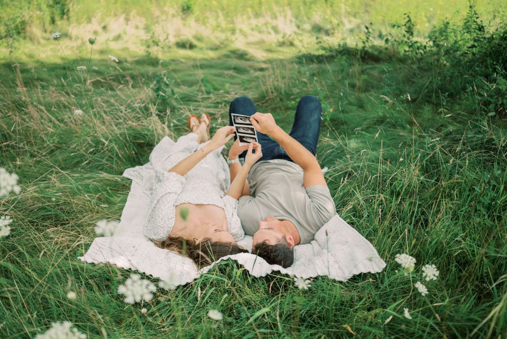 Couple relaxing on blanket in meadow taking photos together on summer day.