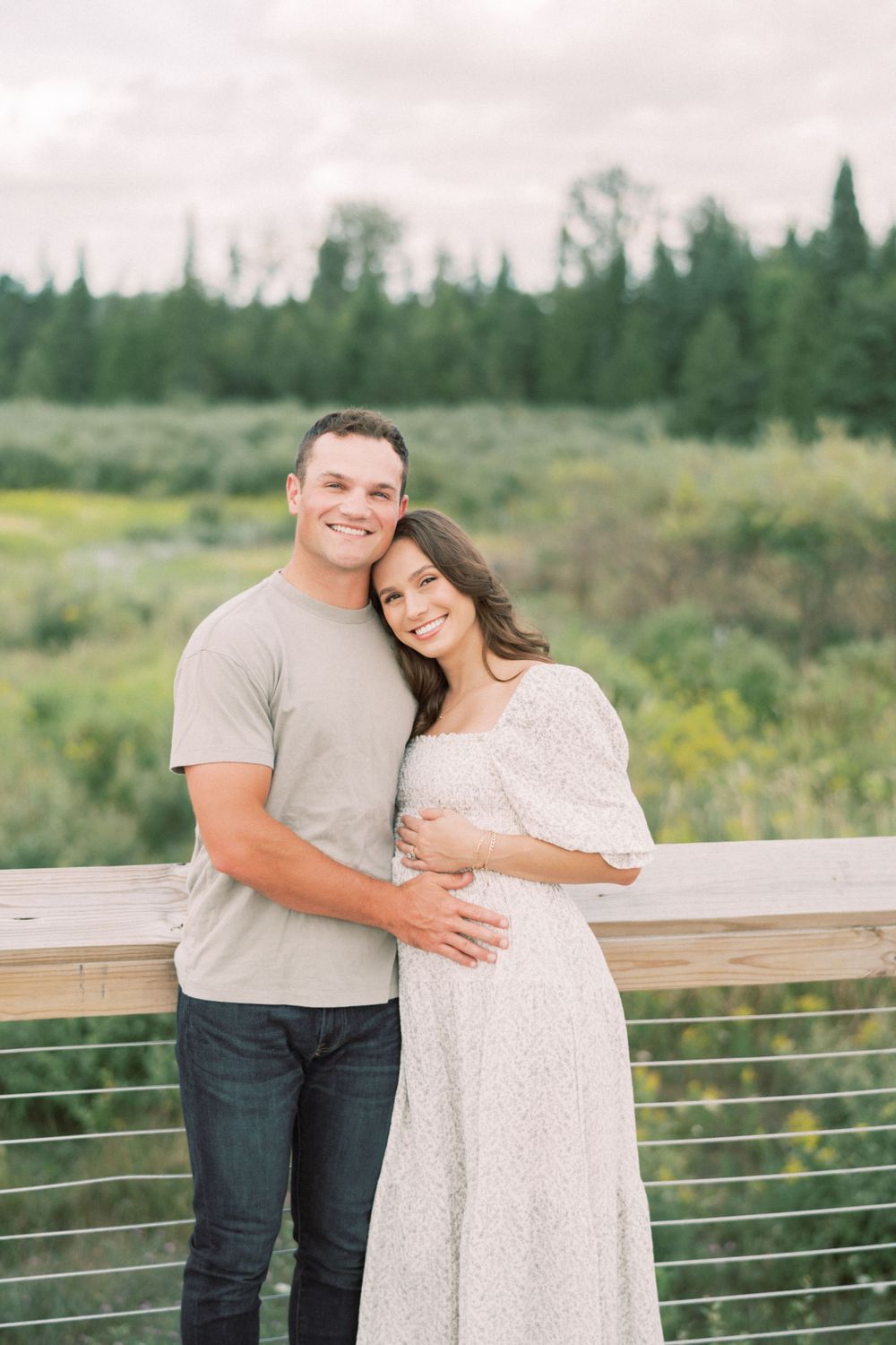 Happy expectant couple embrace on wooden deck with forest backdrop.