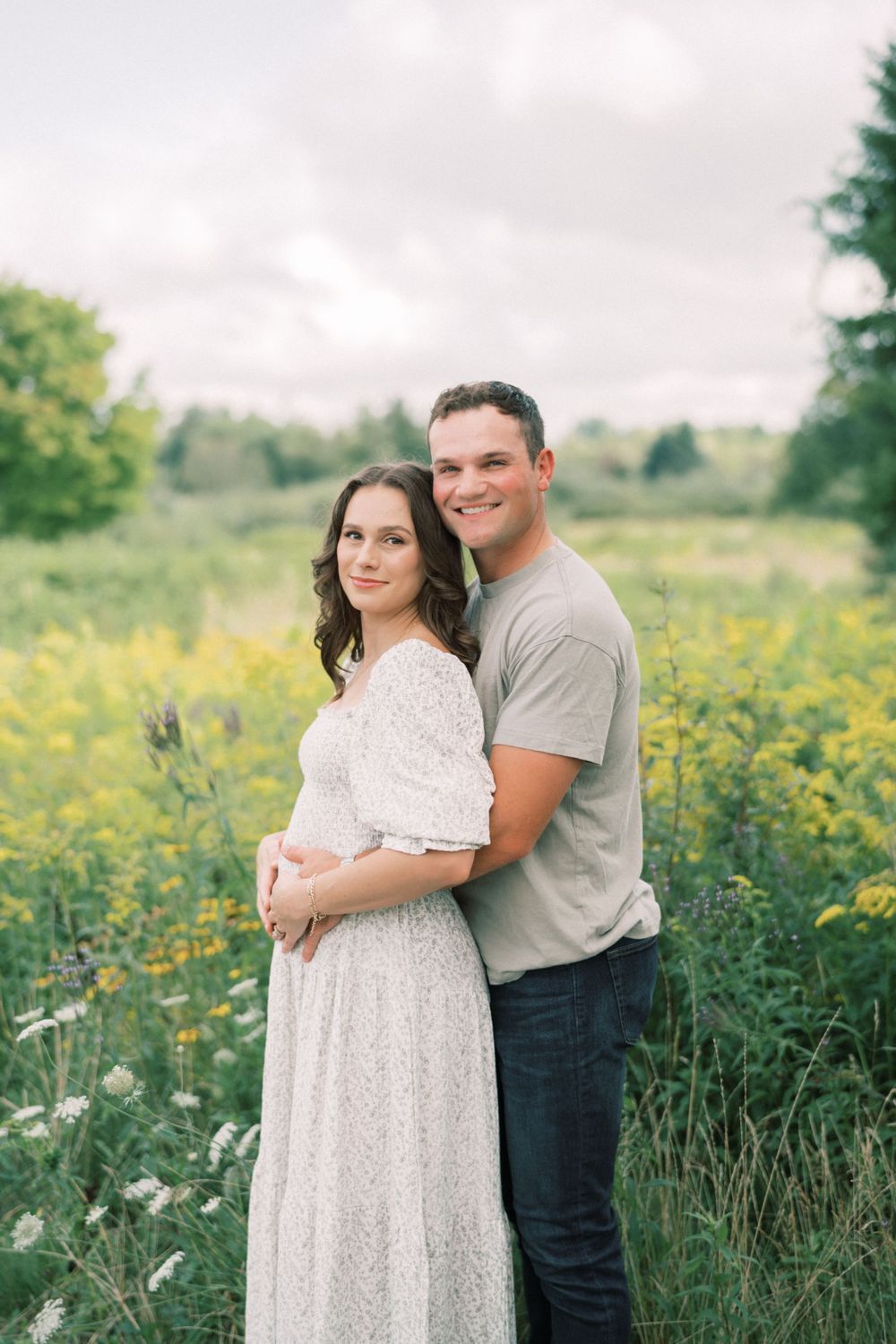 Expectant couple shares tender moment in field of wildflowers during maternity photoshoot.